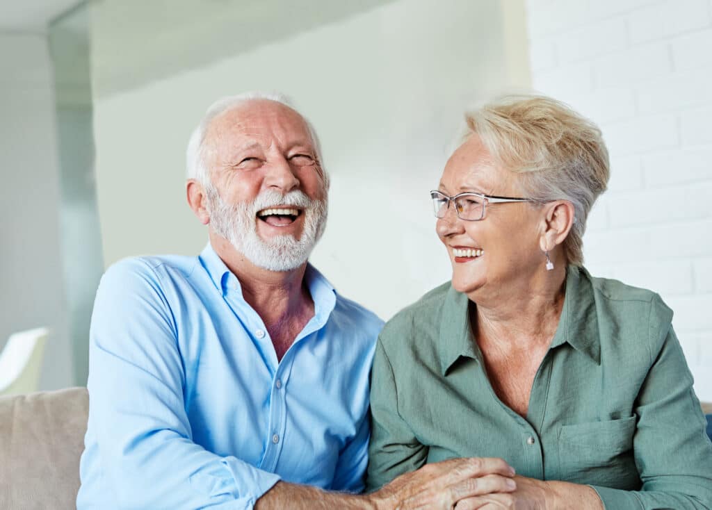 An elderly couple is sitting together, laughing joyfully.