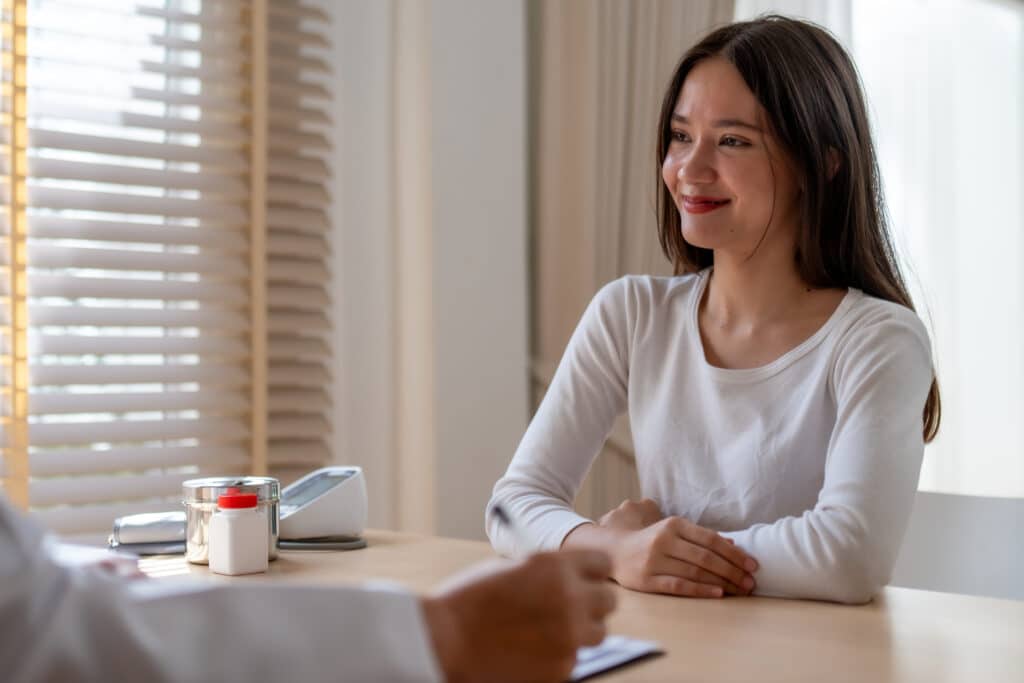 A young woman smiles while talking to a doctor at a desk