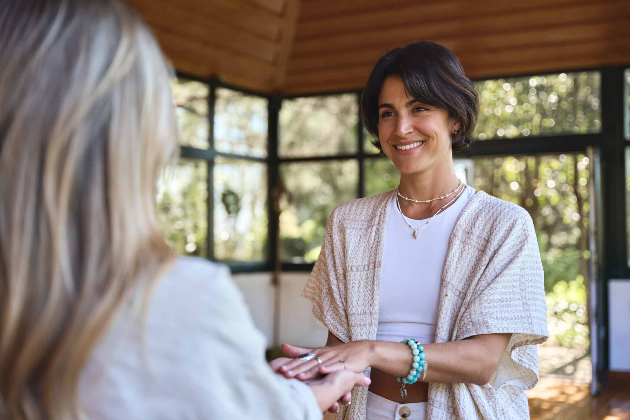 A woman smiles warmly while holding another person’s hands.