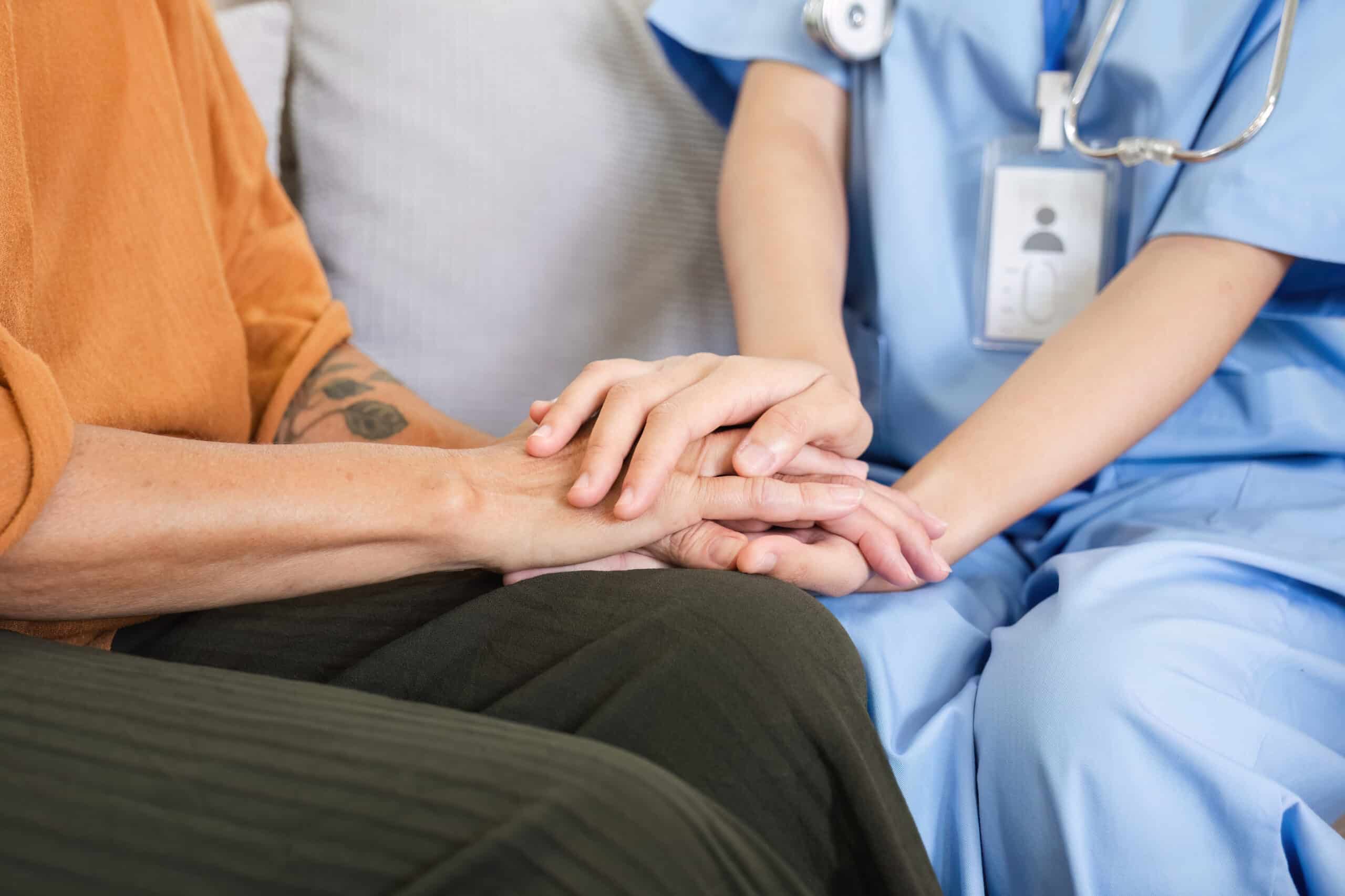 A nurse gently holds a patient’s hand in support.