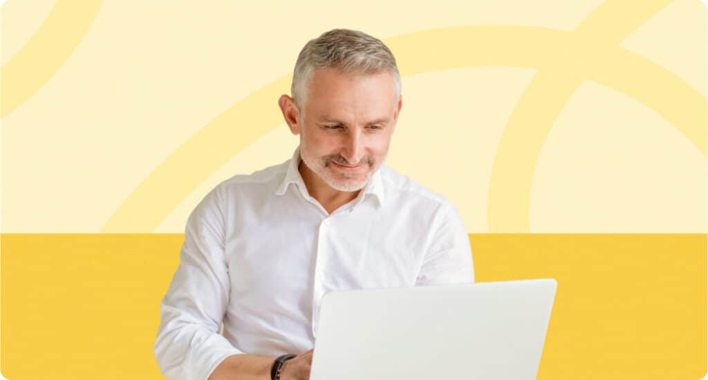 A gray-haired man in a white shirt looks at a laptop.