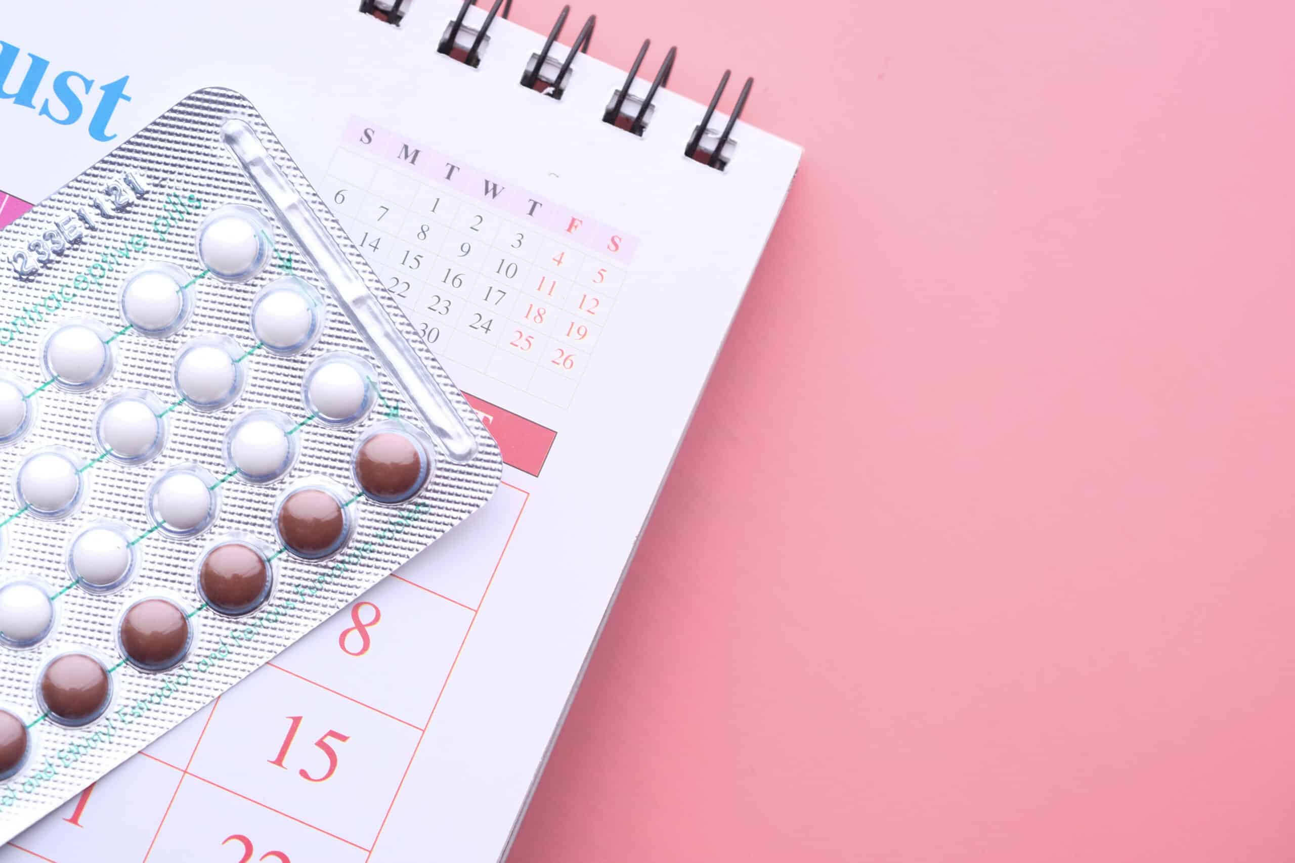 birth control pills , calendar and notepad on table .