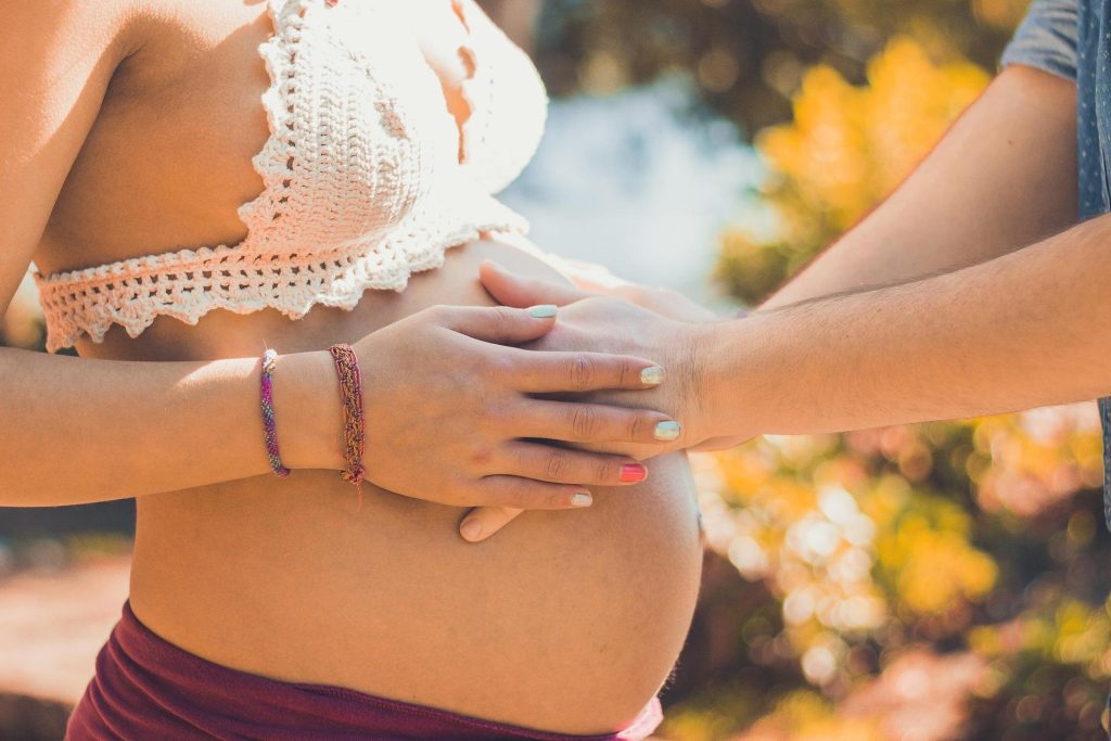 Hands gently resting on a pregnant belly in a warm outdoor setting.