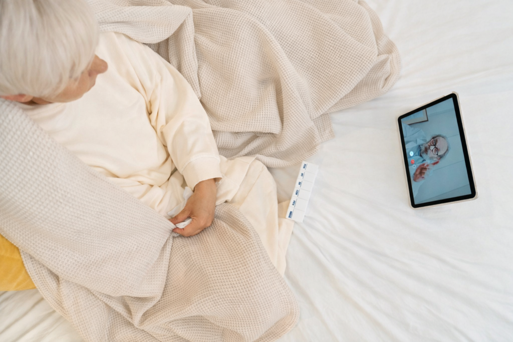 Elderly person on a bed having a video call with a doctor beside a pill organizer.