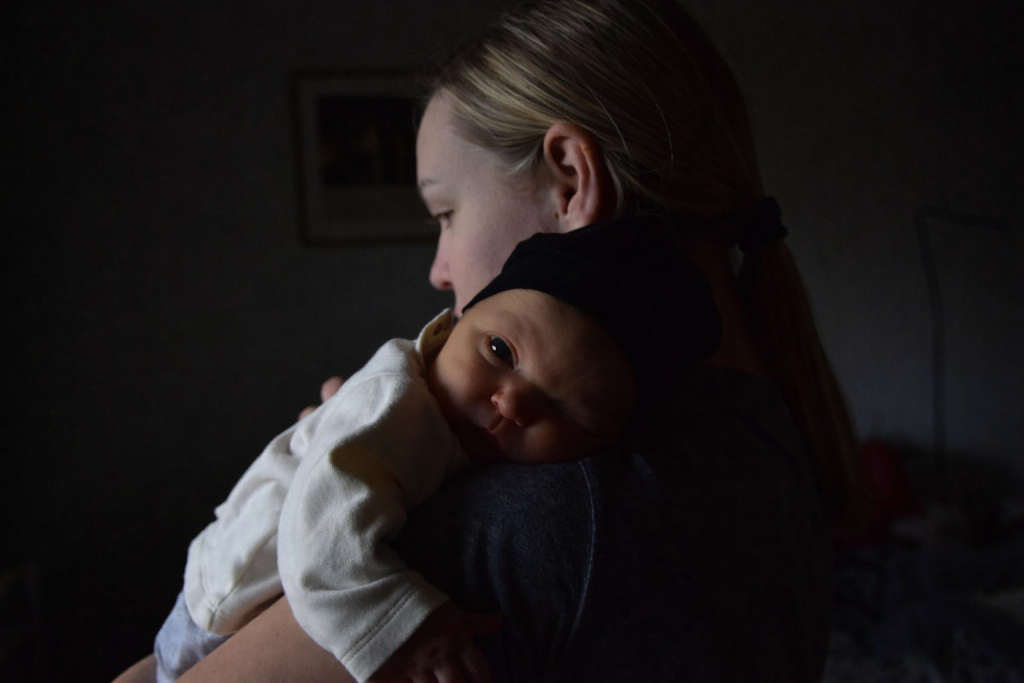 Person holding a baby over their shoulder in a dimly lit room.