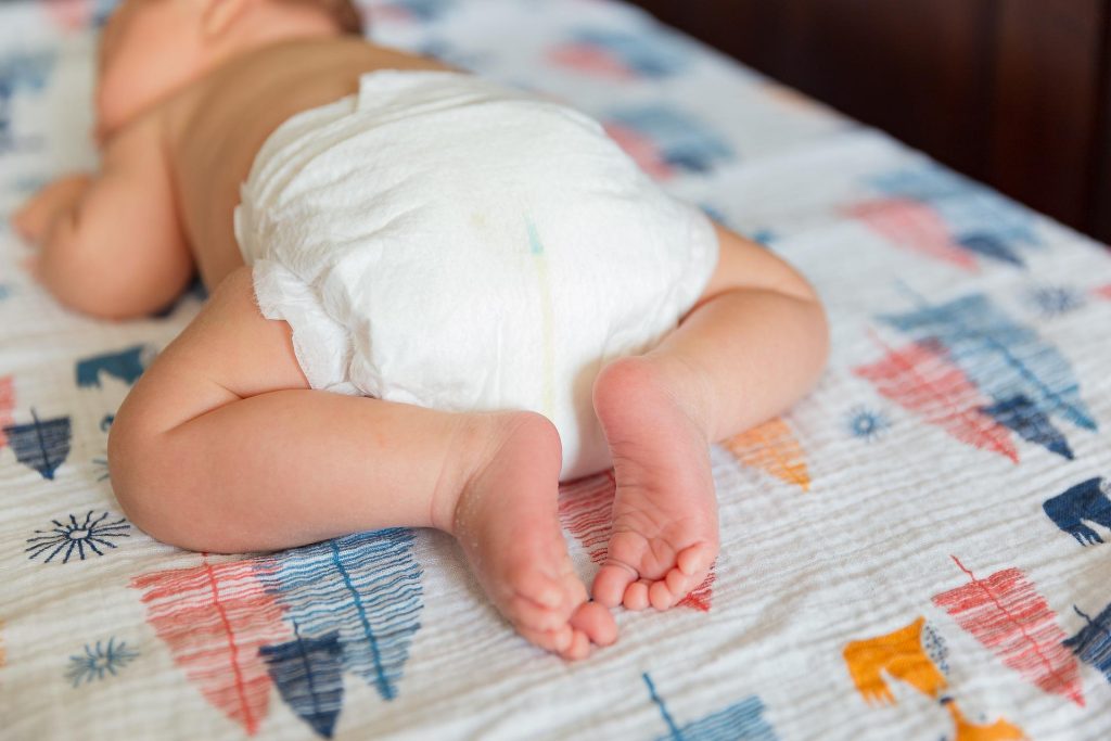 Baby lying on a patterned blanket wearing only a diaper.