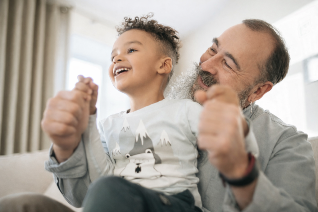 Older adult smiling while holding hands with a young child indoors.